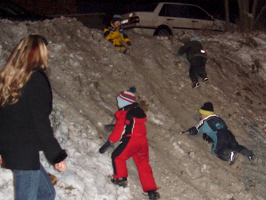 Weihnachtsbaumfeuer - Kinder rutschen im Schnee die Böschung herunter