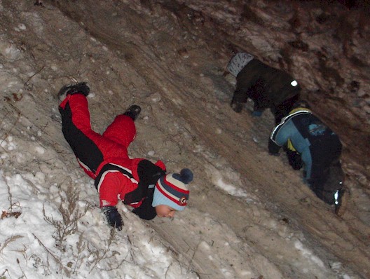 Weihnachtsbaumfeuer - Kinder rutschen im Schnee die Böschung herunter