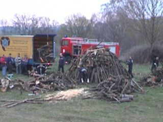 Die Kameraden beim Vorbereiten des Osterfeuers, eingroßer Holzstapel, der LKW und im Hintergrund das Tanklöschfahrzeug